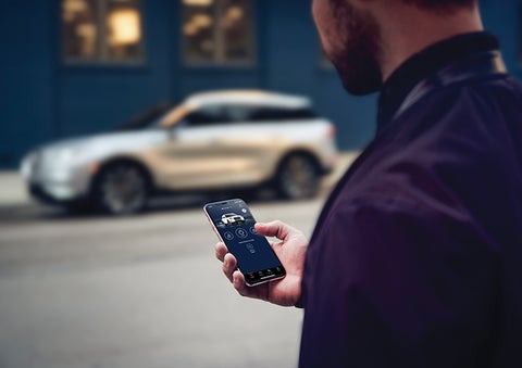 A person is shown interacting with a smartphone to connect to a Lincoln vehicle across the street. | Beck Lincoln in Palatka FL